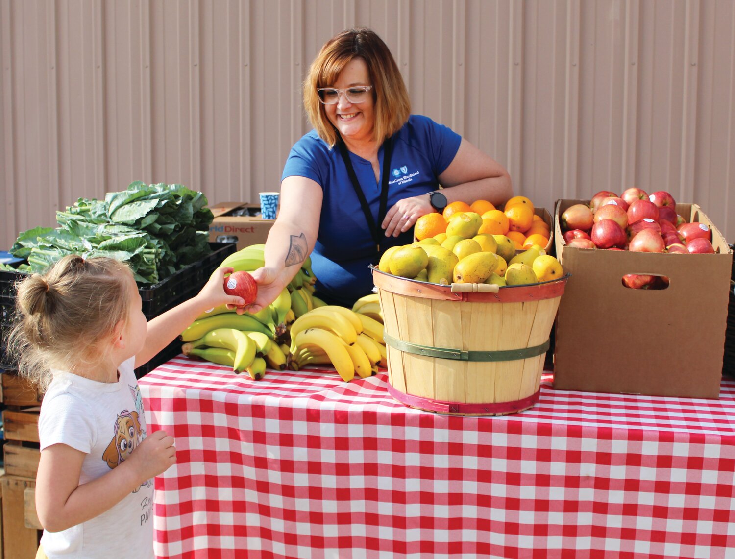 Four-year-old Ellison Wagoner gets fresh produce from Blue Cross and Blue Shield’s Community Relations Coordinator Heather Briggs, at the free produce market BCBS sponsored for the Celebrate Families event.